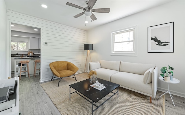 living room with ceiling fan, light hardwood / wood-style flooring, and wood walls