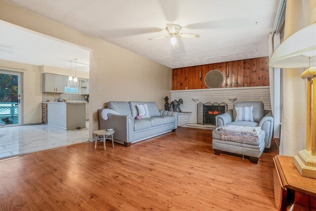 living room featuring a brick fireplace, ceiling fan, wooden walls, and light hardwood / wood-style flooring