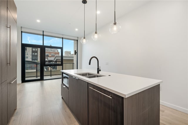 kitchen featuring stainless steel microwave, sink, a kitchen island with sink, pendant lighting, and light hardwood / wood-style flooring