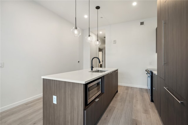 kitchen featuring light hardwood / wood-style floors, sink, appliances with stainless steel finishes, an island with sink, and pendant lighting