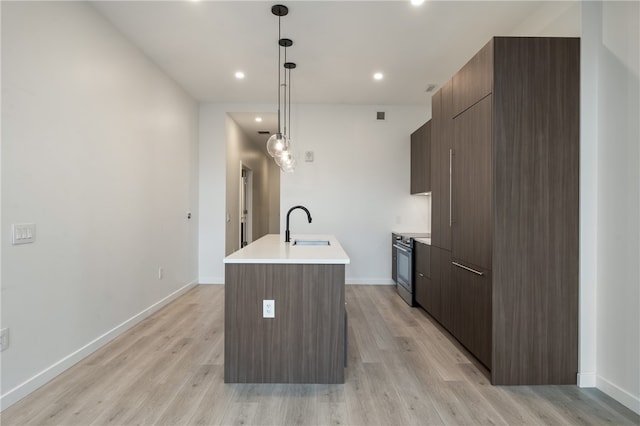 kitchen featuring stainless steel range with electric stovetop, sink, an island with sink, pendant lighting, and light hardwood / wood-style flooring