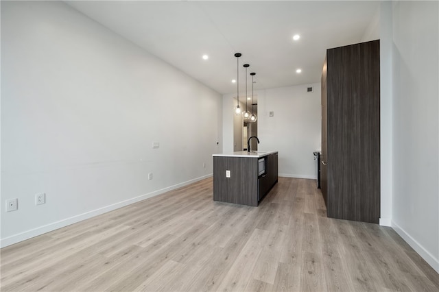 kitchen with hanging light fixtures, a center island with sink, light hardwood / wood-style flooring, and dark brown cabinetry