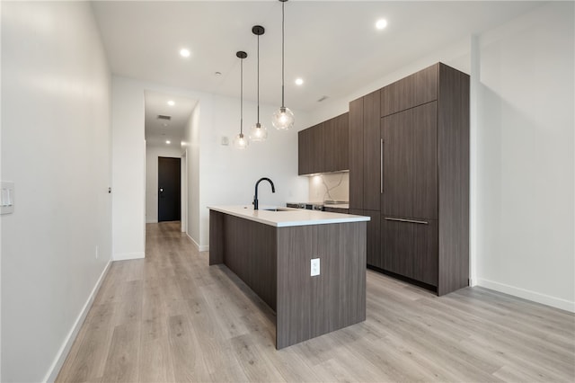 kitchen featuring light hardwood / wood-style floors, sink, dark brown cabinets, a kitchen island with sink, and pendant lighting