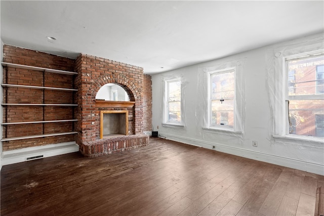 unfurnished living room featuring built in features, a wealth of natural light, hardwood / wood-style floors, and a brick fireplace