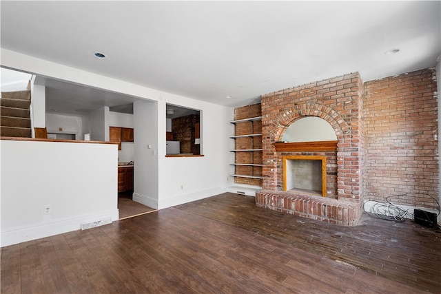 unfurnished living room with a fireplace, built in features, wood-type flooring, and brick wall