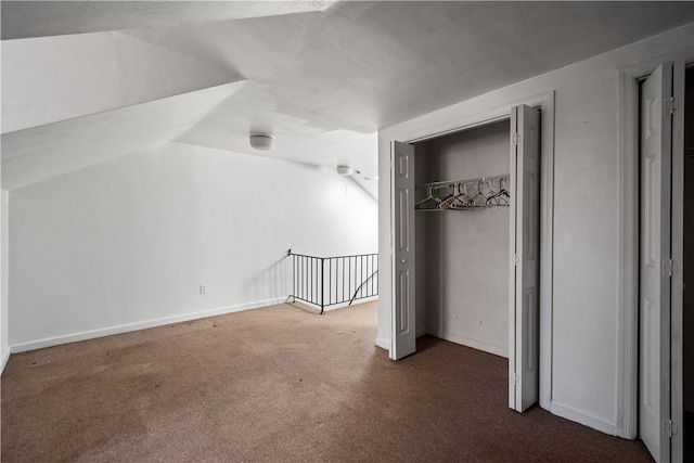 unfurnished bedroom with vaulted ceiling, a textured ceiling, a closet, and dark carpet