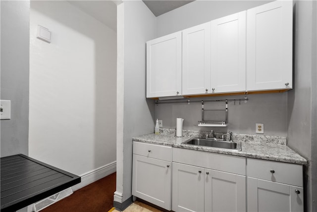 kitchen with white cabinetry, sink, and light stone counters