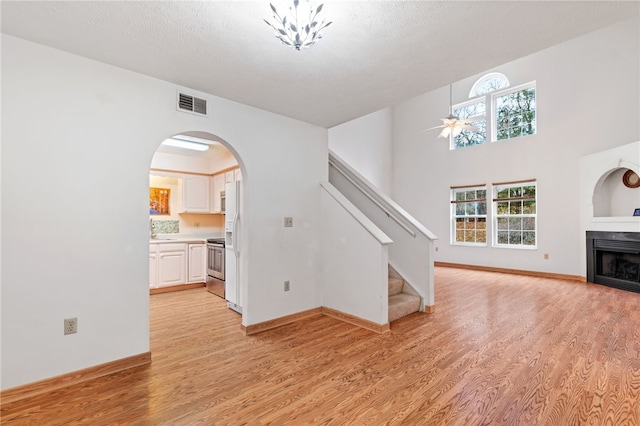 unfurnished living room with a textured ceiling, light wood-type flooring, and ceiling fan