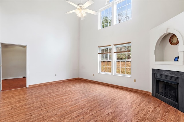 unfurnished living room featuring ceiling fan, a wealth of natural light, a high ceiling, and light hardwood / wood-style floors