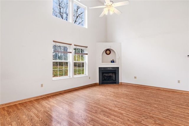 unfurnished living room featuring a towering ceiling, wood-type flooring, and ceiling fan