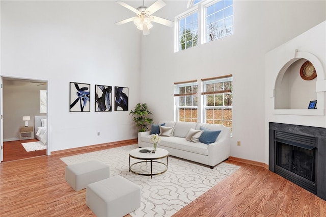 living room with a high ceiling, ceiling fan, and light hardwood / wood-style flooring