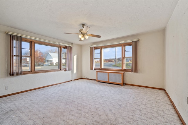 carpeted empty room with radiator heating unit, a textured ceiling, and ceiling fan