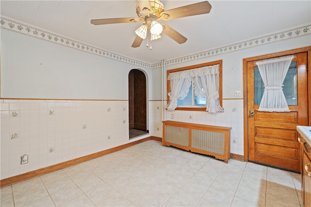 tiled empty room with tile walls, radiator heating unit, and ceiling fan