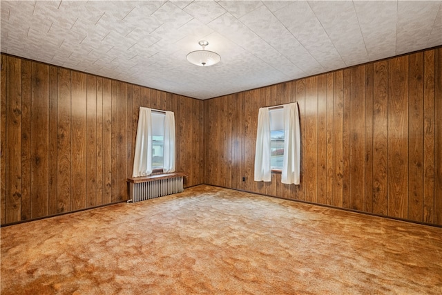 empty room with wood walls, radiator heating unit, and carpet