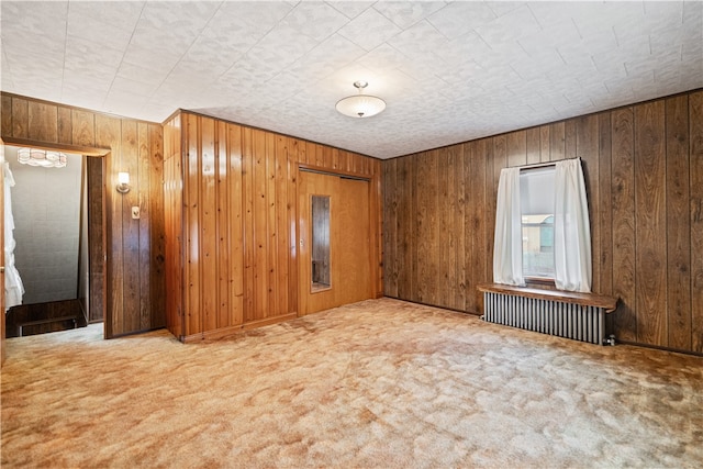 empty room with radiator heating unit, carpet floors, and wooden walls