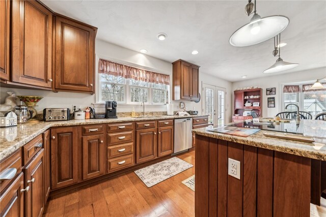 kitchen featuring light stone countertops, hanging light fixtures, sink, light hardwood / wood-style floors, and stainless steel dishwasher