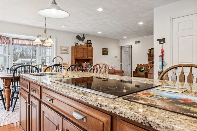 kitchen featuring light stone countertops, hanging light fixtures, light hardwood / wood-style flooring, a notable chandelier, and black electric stovetop