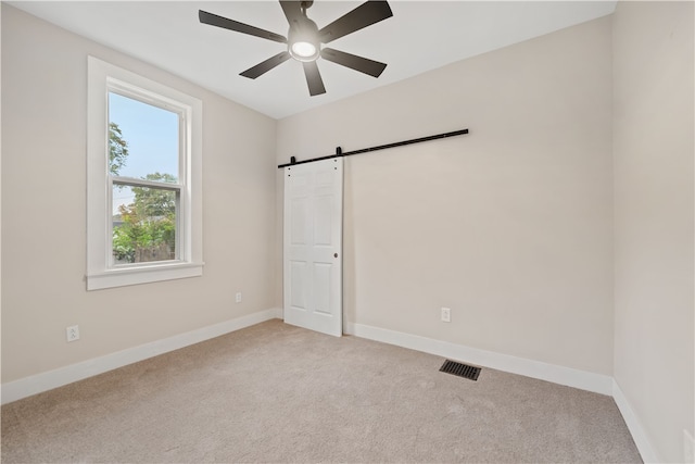 carpeted empty room featuring a barn door and ceiling fan