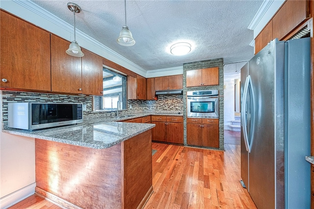 kitchen featuring stainless steel appliances, kitchen peninsula, ornamental molding, hanging light fixtures, and light wood-type flooring