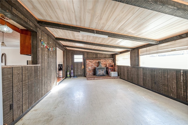 unfurnished living room with lofted ceiling with beams, wood walls, a wood stove, and wooden ceiling