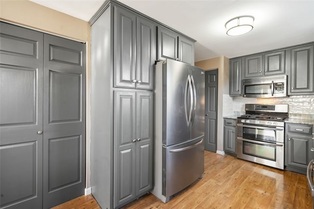 kitchen featuring gray cabinetry, backsplash, light hardwood / wood-style flooring, appliances with stainless steel finishes, and light stone counters