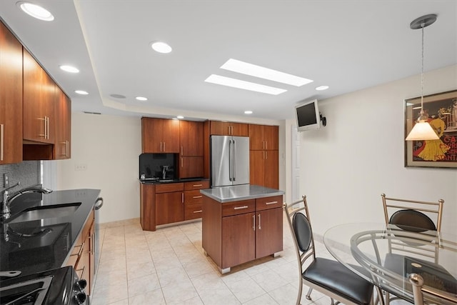 kitchen featuring stainless steel counters, high end refrigerator, backsplash, decorative light fixtures, and sink