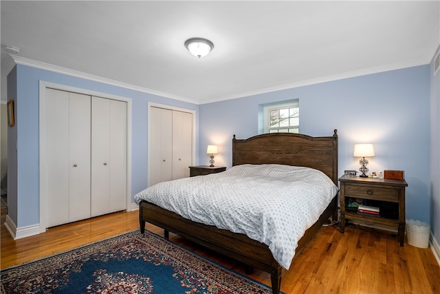 bedroom featuring wood-type flooring, crown molding, and two closets