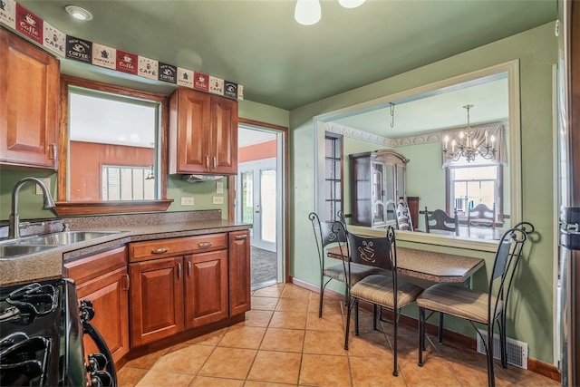 kitchen with light tile patterned flooring, sink, an inviting chandelier, hanging light fixtures, and black gas stove