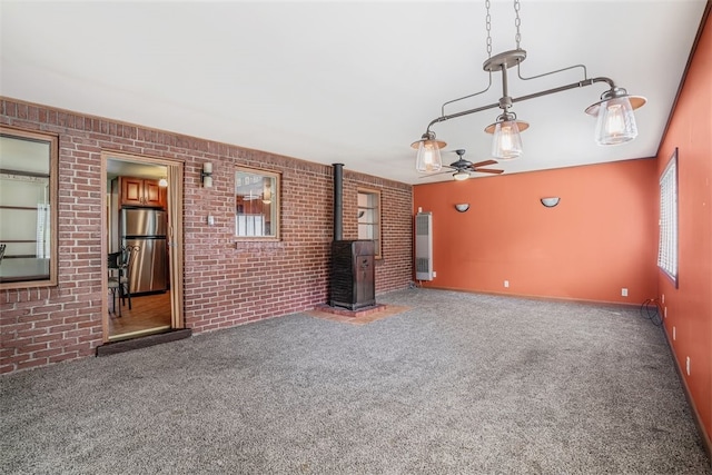 unfurnished living room featuring brick wall, ceiling fan, and carpet floors