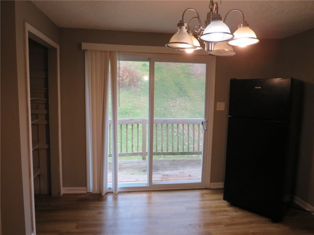 unfurnished dining area featuring wood-type flooring, a textured ceiling, and an inviting chandelier