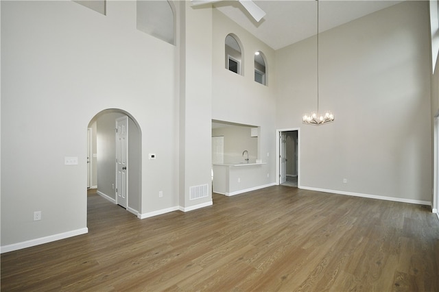 unfurnished living room featuring hardwood / wood-style floors, a notable chandelier, sink, and a high ceiling