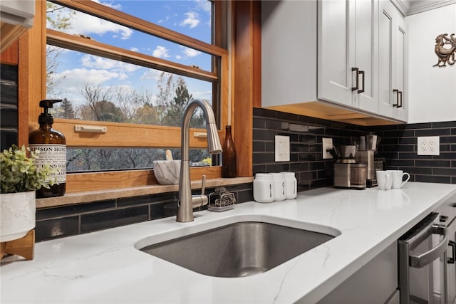 kitchen featuring dishwasher, sink, backsplash, light stone countertops, and white cabinetry