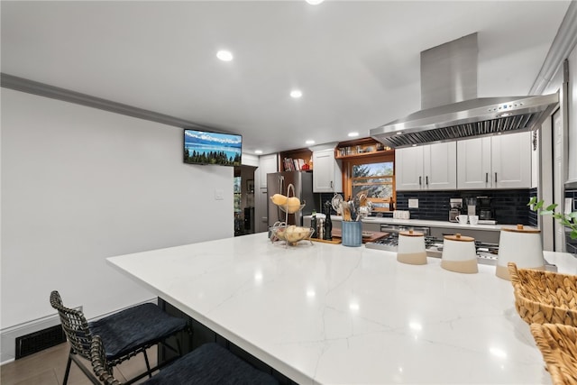 kitchen with stainless steel appliances, ornamental molding, a kitchen breakfast bar, island range hood, and backsplash