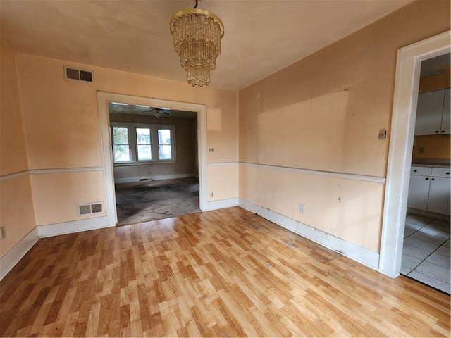 empty room with light hardwood / wood-style floors and ceiling fan with notable chandelier