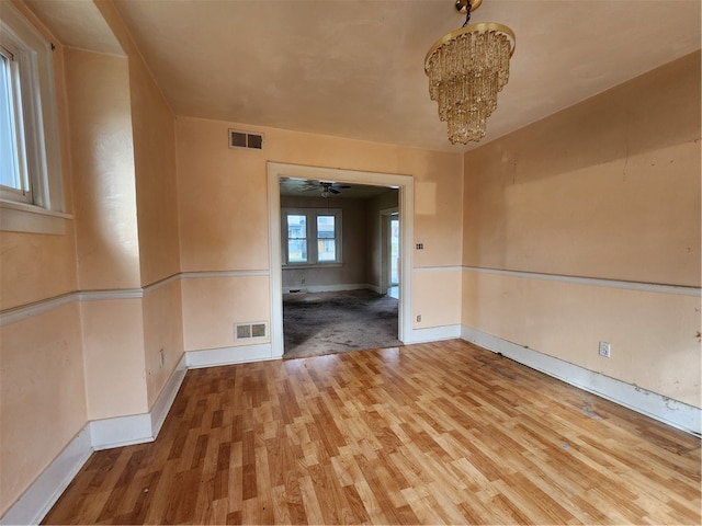 unfurnished room with ceiling fan with notable chandelier and hardwood / wood-style floors