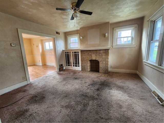 unfurnished living room with ceiling fan, light colored carpet, a tile fireplace, and a textured ceiling