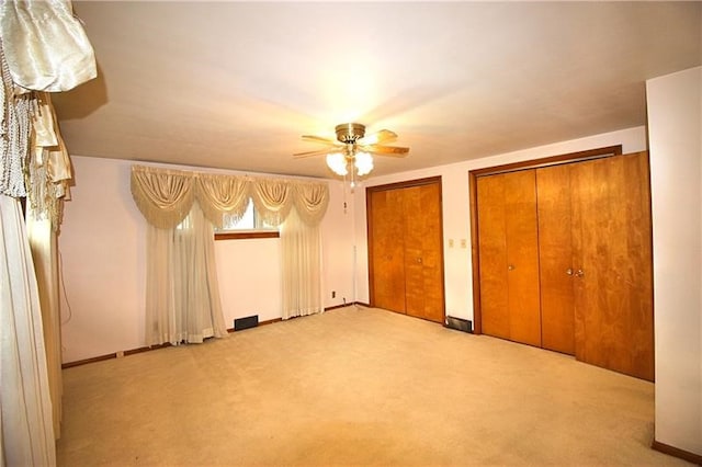 unfurnished bedroom with multiple closets, light colored carpet, and ceiling fan