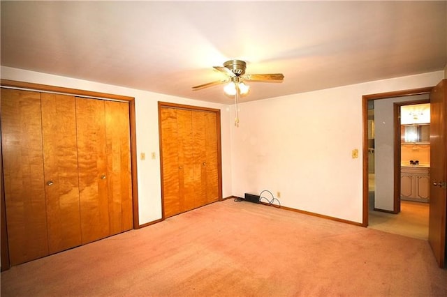 unfurnished bedroom featuring ceiling fan, light carpet, and multiple closets