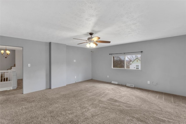 carpeted spare room featuring ceiling fan with notable chandelier and a textured ceiling