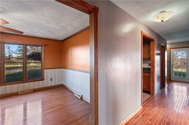 hall with light wood-type flooring, a wealth of natural light, and crown molding