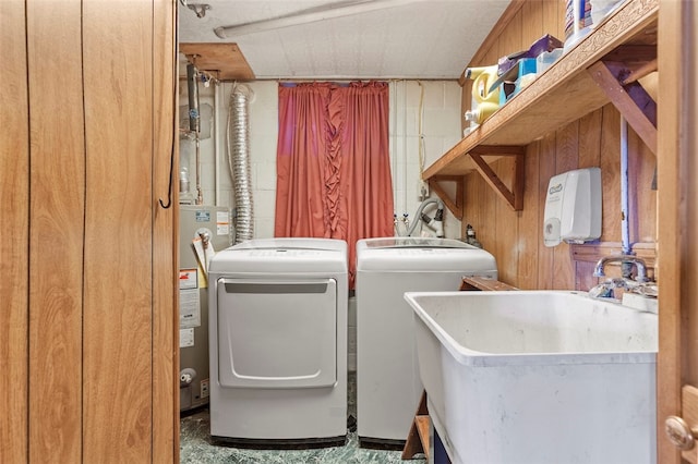 laundry room with laundry area, wooden walls, washer and dryer, water heater, and a sink