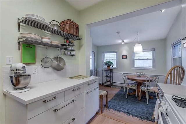 kitchen with radiator heating unit, light wood-type flooring, pendant lighting, decorative backsplash, and white cabinets