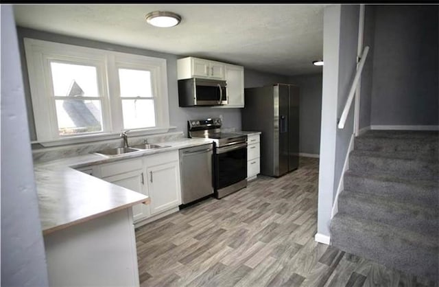 kitchen with stainless steel appliances, white cabinets, sink, and light wood-type flooring