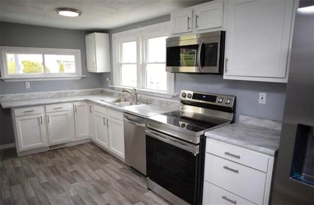 kitchen with stainless steel appliances, wood-type flooring, white cabinetry, and sink