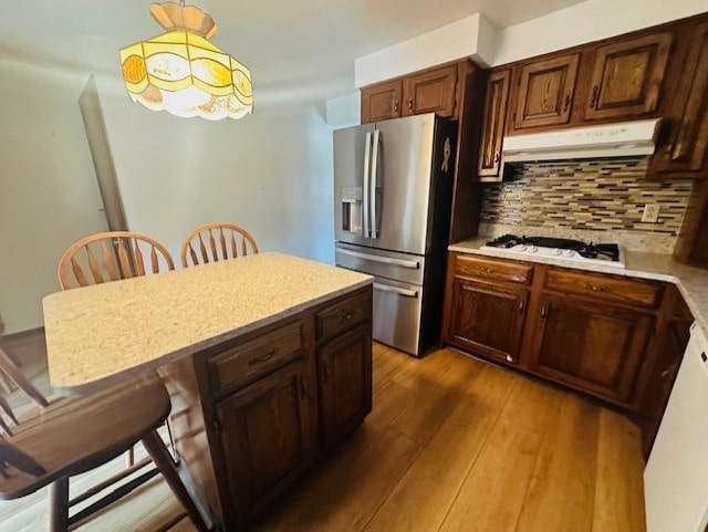 kitchen with white gas cooktop, stainless steel fridge, decorative light fixtures, a kitchen bar, and hardwood / wood-style floors