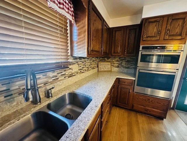 kitchen with decorative backsplash, sink, double oven, light stone countertops, and light hardwood / wood-style flooring