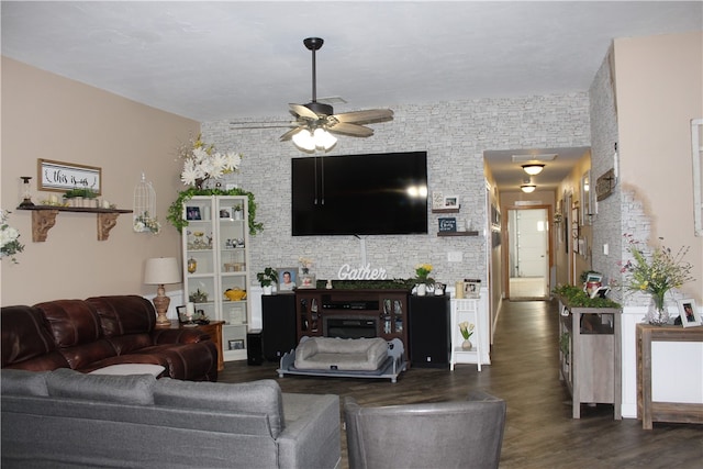 living room featuring a fireplace, dark wood-type flooring, ceiling fan, and brick wall