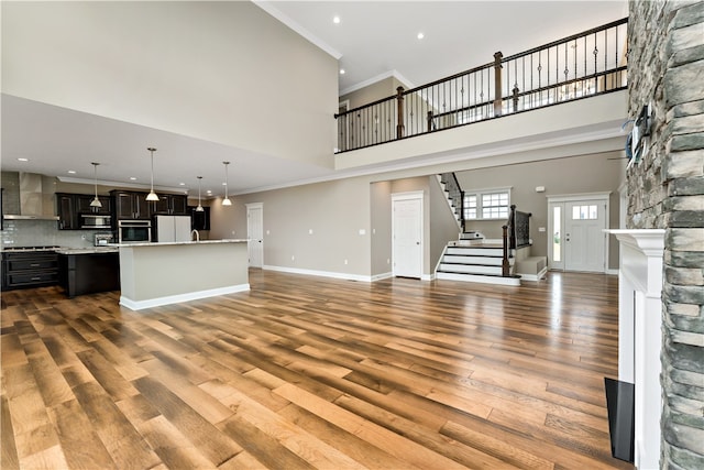 unfurnished living room with crown molding, dark hardwood / wood-style floors, a high ceiling, and a stone fireplace