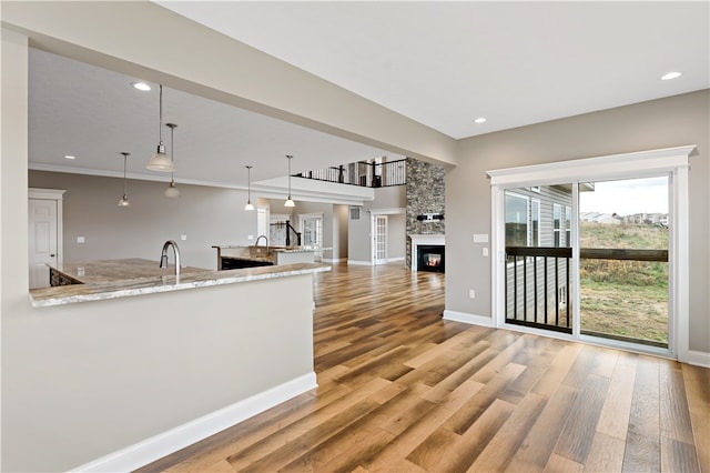 kitchen with a stone fireplace, light stone counters, hanging light fixtures, hardwood / wood-style flooring, and crown molding