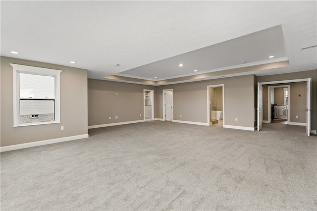 spare room with washer / clothes dryer, light colored carpet, ornamental molding, and a raised ceiling